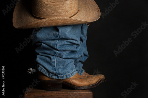 Jeans and Cowboy Hat – A close up of a cowboy boot, spur, and hat against a dark background