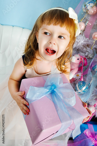 Little girl smiling with present near the Christmas tree