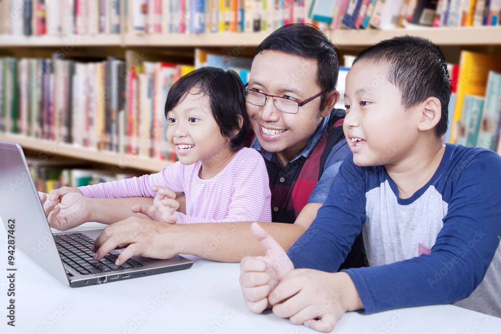 Obraz premium Two children using laptop with teacher in library
