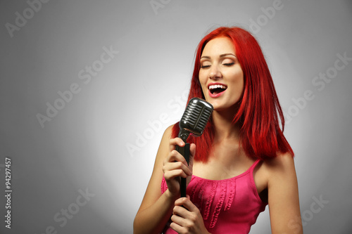 Beautiful young woman with microphone on gray background