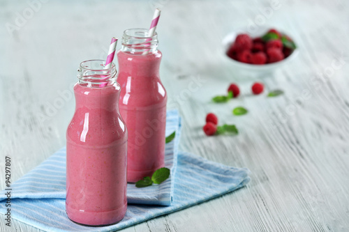 Bottles of raspberry milk shake with berries on wooden table close up