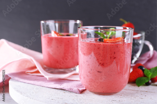 Glasses of berry smoothie on wooden table on dark background