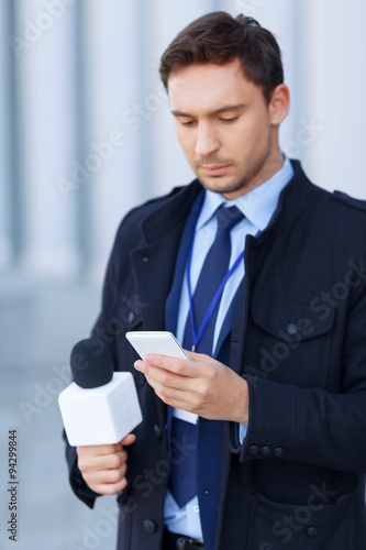 Handsome newsgatherer is busy working on the phone.  photo