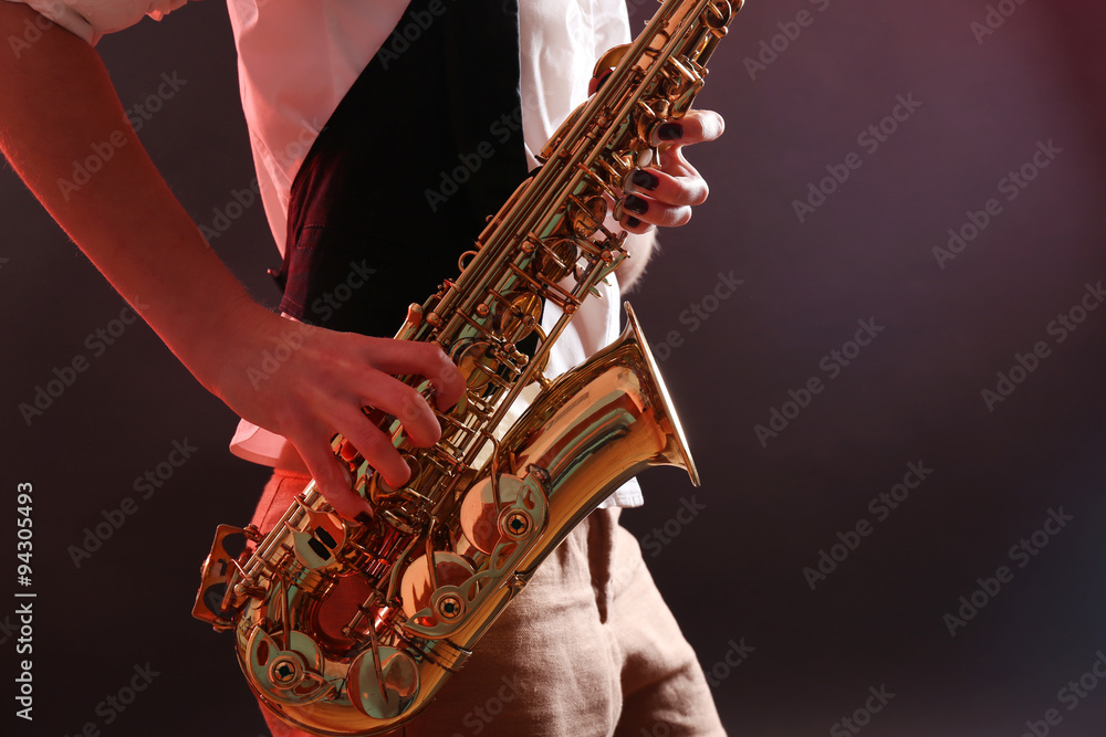Obraz premium Saxophone in female hands on dark background, close up
