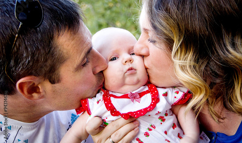 Parents kissing baby. Mom and Dad kissing baby on the cheek - the image of a happy family.