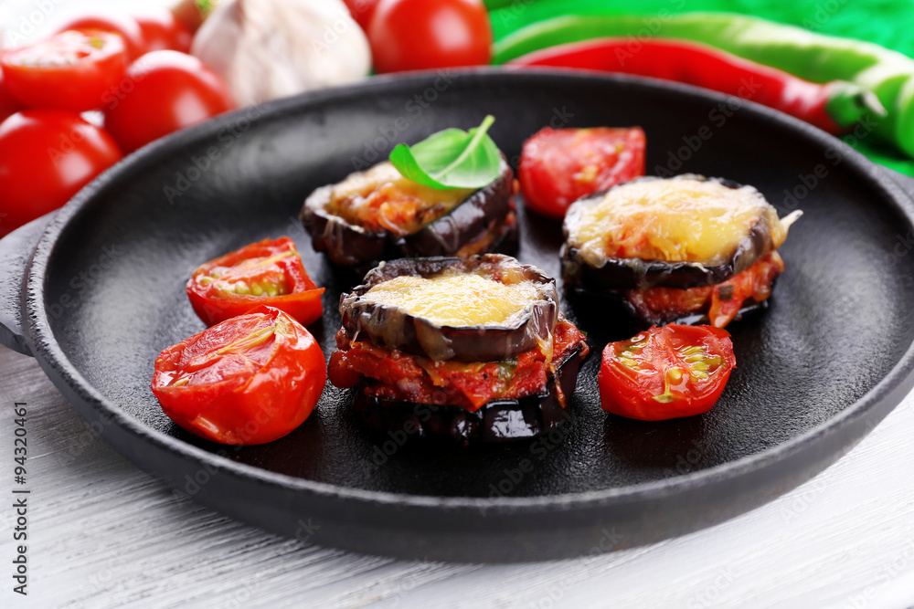 Dish of eggplant with cherry tomatoes and cheese in black pan on wooden table, closeup Dish of eggplant with cherry tomatoes and cheese in black pan on wooden table, closeup