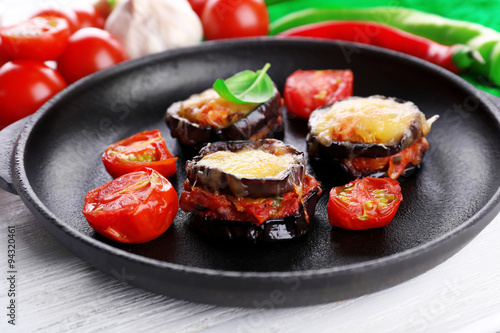 Dish of eggplant with cherry tomatoes and cheese in black pan on wooden table, closeup