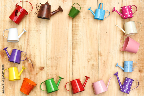 small colorful watering cans and buckets arranged as a picture frame on wood plank background