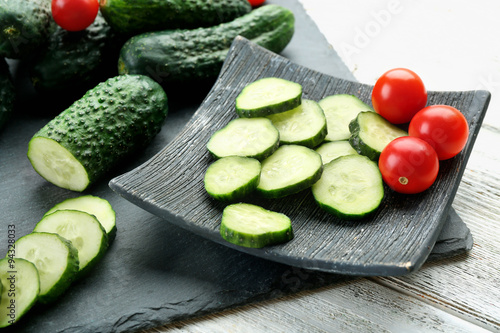 Sliced cucumbers with tomatoes on black plank on wooden background