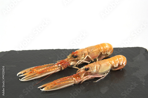 Fresh prawns on a black board. Isolated board with two prawns. Background white. Nephrops norvegicus also know as Norway lobster, Dublin Bay prawn, langoustine,  langostino or scampi. photo