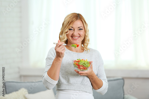 Beautiful woman with salad on home interior background