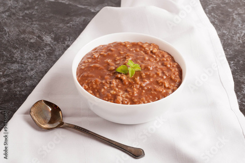 Chocolate porridge with banana in white bowl, decorated mint