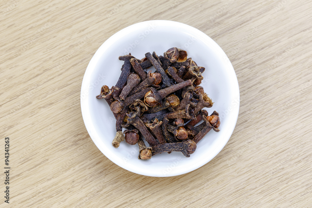 Dry clove in white bowl on wooden table Dry clove in white bowl on wooden table
