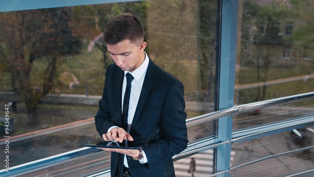 Young businessman working with tablet at the window: then smiling at the camera Young businessman working with tablet at the window: then smiling at the camera