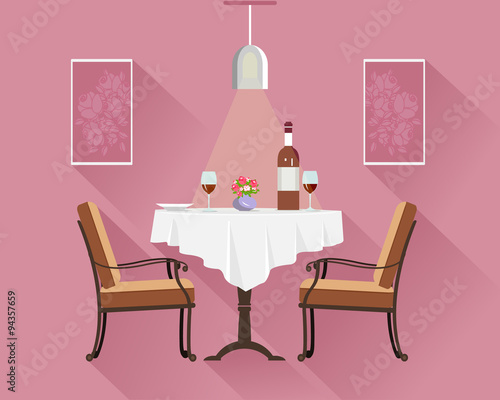  Flat style round restaurant table for two with white cloth, wine glasses, bottle of wine, plate and vase with flowers. Restaurant interior with dinner table, chairs, lamp and pictures.