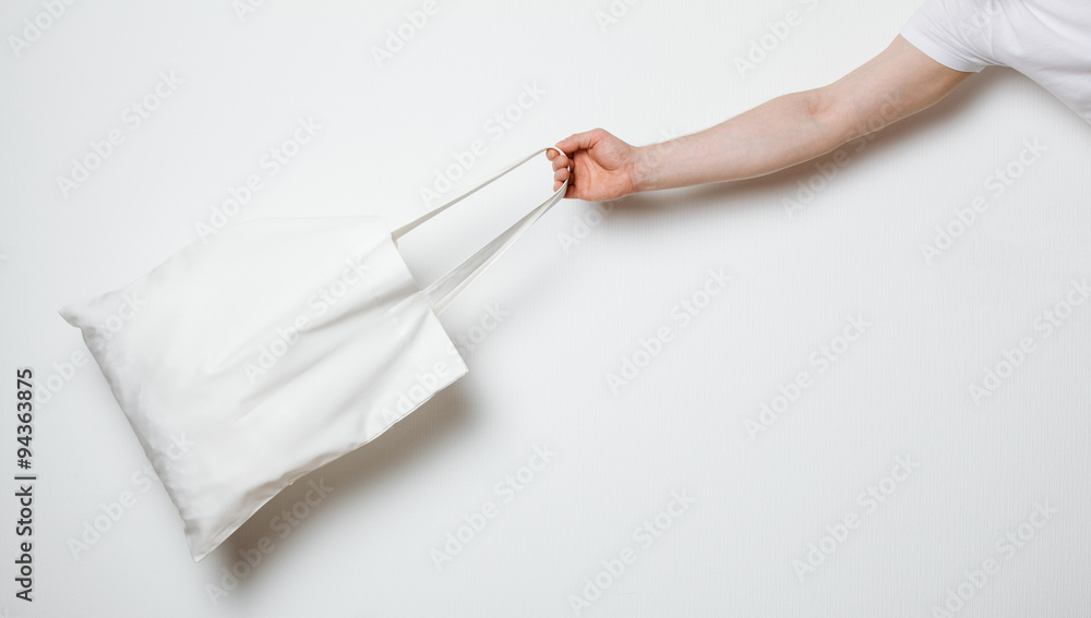 Male hand holding white textile bag Male hand holding white textile bag