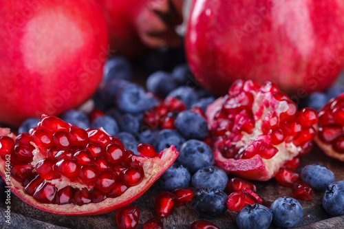 Juicy pomegranates,whole and broken and blueberries on wooden background.selective focus.