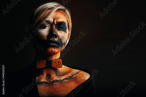 halloween portrait of body art pumpkin girl with pumpkin bowtie on black background. Real greasepaint and face art makeup