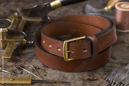 Leather goods craftsman's tools and a ready belt on a dirty work bench