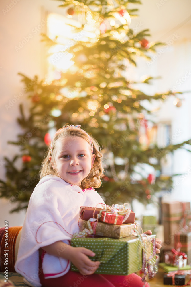 next the Christmas lighted tree, girl with arms full of gifts next the Christmas lighted tree, girl with arms full of gifts