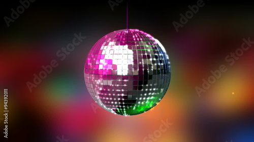 A closeup of a colorful reflective disco mirrorball with glinting highlights spinning slowly on a blurry colored background photo