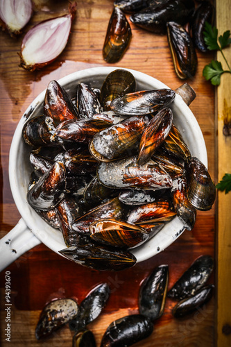Fresh mussels in old colander on rustic wooden background, top view