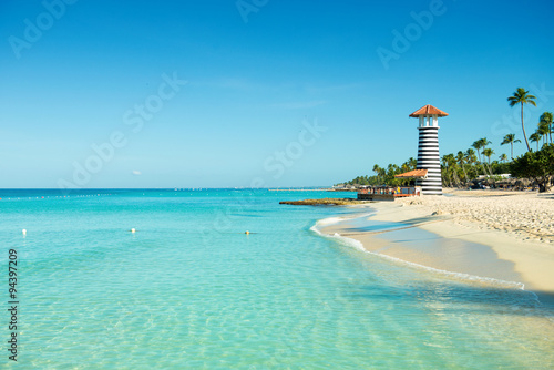 Paradise Caribbean landscape. Clear sea, white sand, tropical palm trees and lighthouse on sandy shore