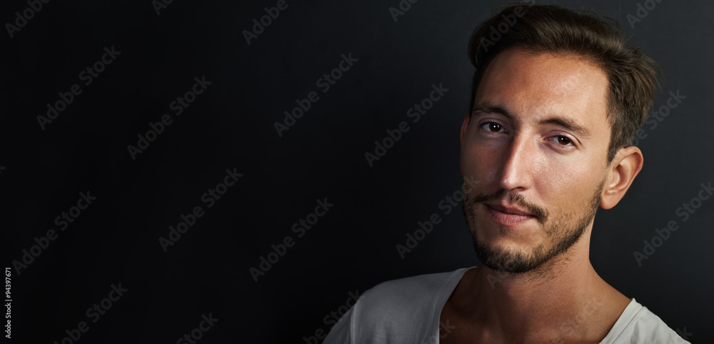 Portrait of handsome young man wearing white tshirt on the black background . Wide