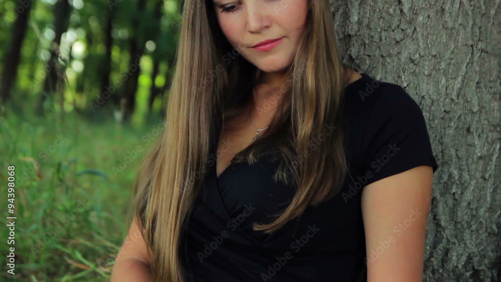 beautiful girl in a dress sits in a park under a tree reading a book in the sun beautiful girl in a dress sits in a park under a tree reading a book in the sun