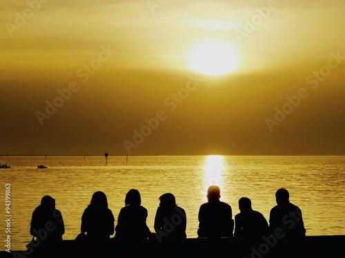 Tourists sitting on the seashore watching sunset