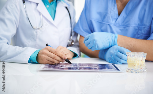 Portrait of female dentist and male surgeon examining teeth x-ray of a patient sitting at the desk in lab.   