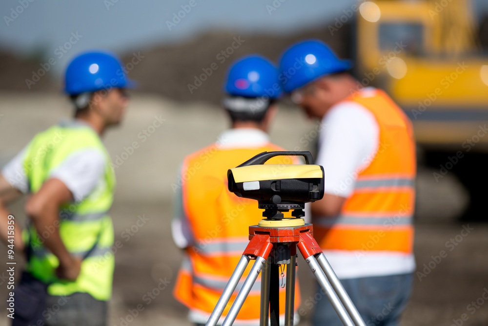 Theodolite and workers at construction site - obrazy, fototapety, plakaty 