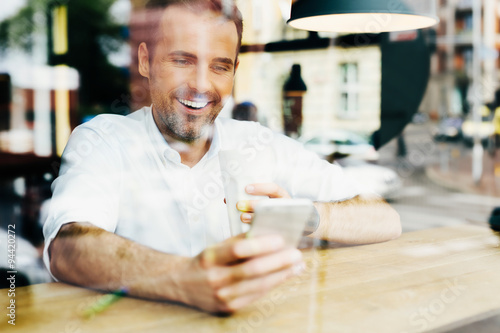 Photo of happy man looking at smartphone in cafe