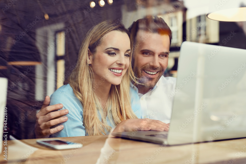 Happy couple at coffee shop looking at laptop Happy couple at coffee shop looking at laptop