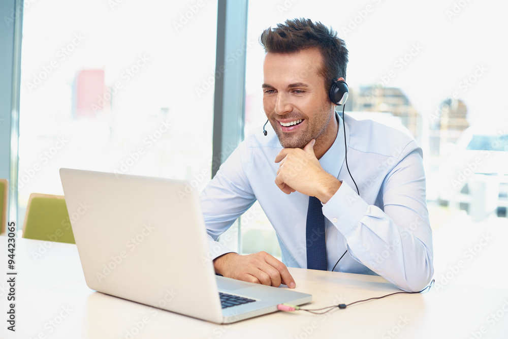 Happy businessman with laptop and headset talking during video c Happy businessman with laptop and headset talking during video c