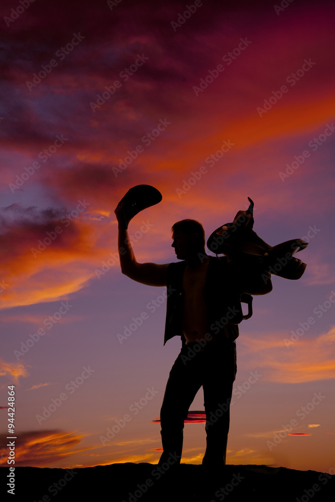 silhouette of a cowboy holding his hat up and a saddle on should