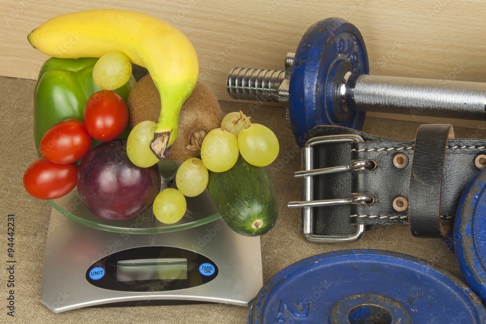 Naklejka premium Chrome dumbbells surrounded with healthy fruits and vegetables on a table. Concept of healthy eating and weight loss. Diet for athletes. 