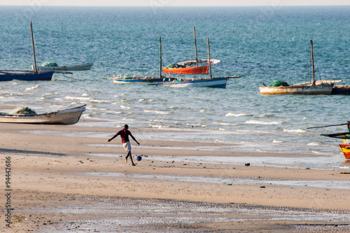 Man plays soccer and in the background sailing boats are anchored at the beach of Vilanculos.
