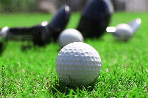 Different golf clubs in a row and balls on a green grass, close up