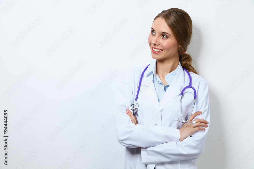 Friendly smiling young female doctor, standing near wall Friendly smiling young female doctor, standing near wall