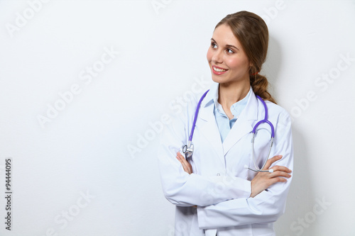 Friendly smiling young female doctor, standing near wall