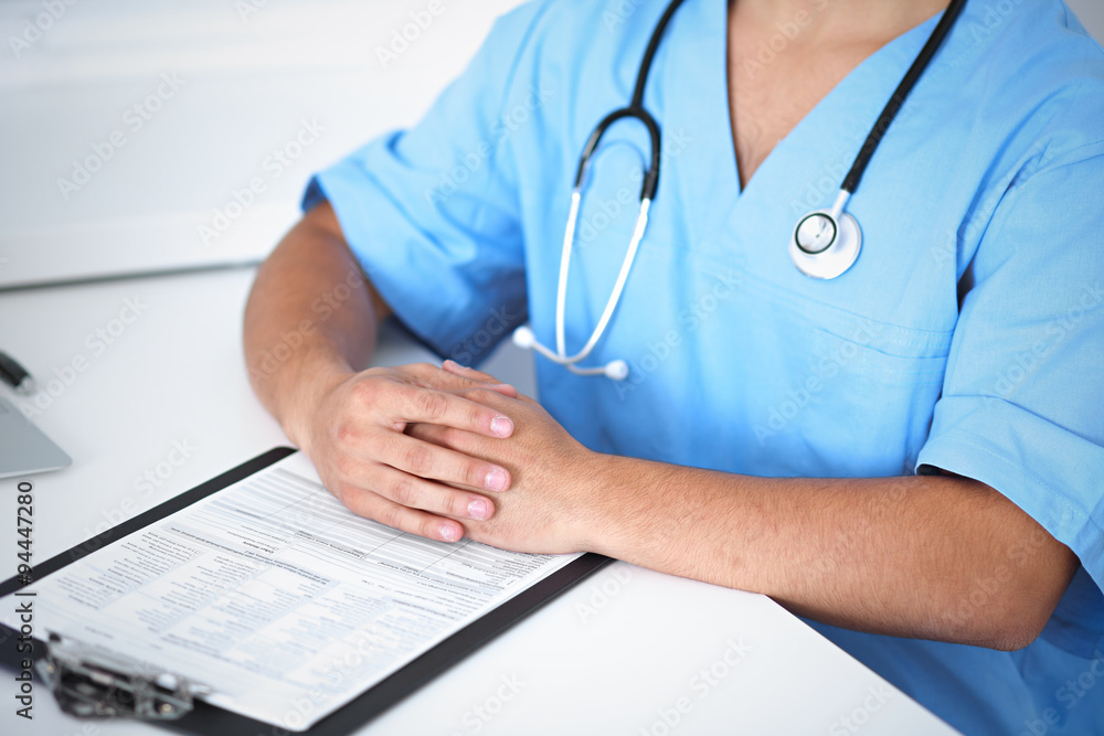 Portrait of unknown male surgeon doctor sitting at the table in hospital office, stethoscope Portrait of unknown male surgeon doctor sitting at the table in hospital office, stethoscope