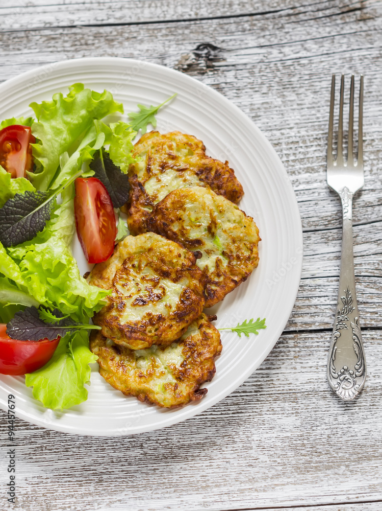 zucchini pancake and fresh vegetable salad on white plate on bright wooden surface zucchini pancake and fresh vegetable salad on white plate on bright wooden surface
