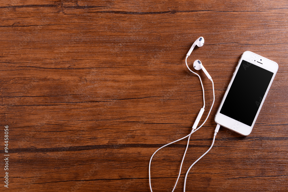 White cellphone with headphones on varnished wooden background White cellphone with headphones on varnished wooden background