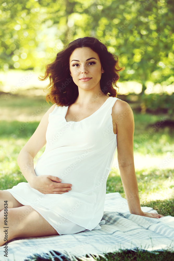 Attractive pregnant woman on white blanket in the park Attractive pregnant woman on white blanket in the park