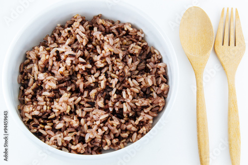 Black rice in bowl and wooden spoon on white background.