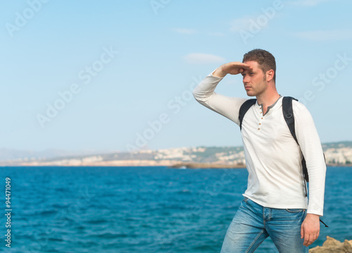 Male tourist with backpack standing near the sea.