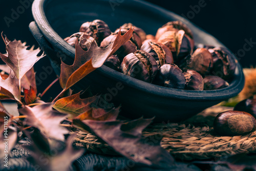 Roasted chestnuts on a rustic wooden table with autumn leaves in the background. photo