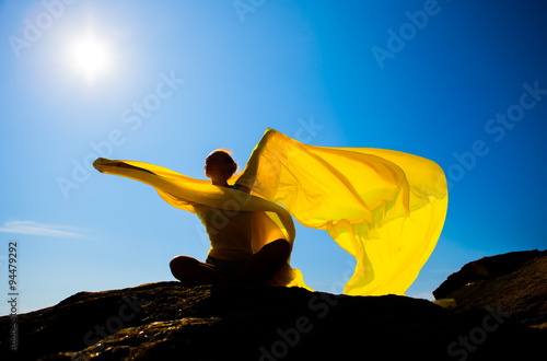 Silhouette of the sports girl with yellow fabric against the sky