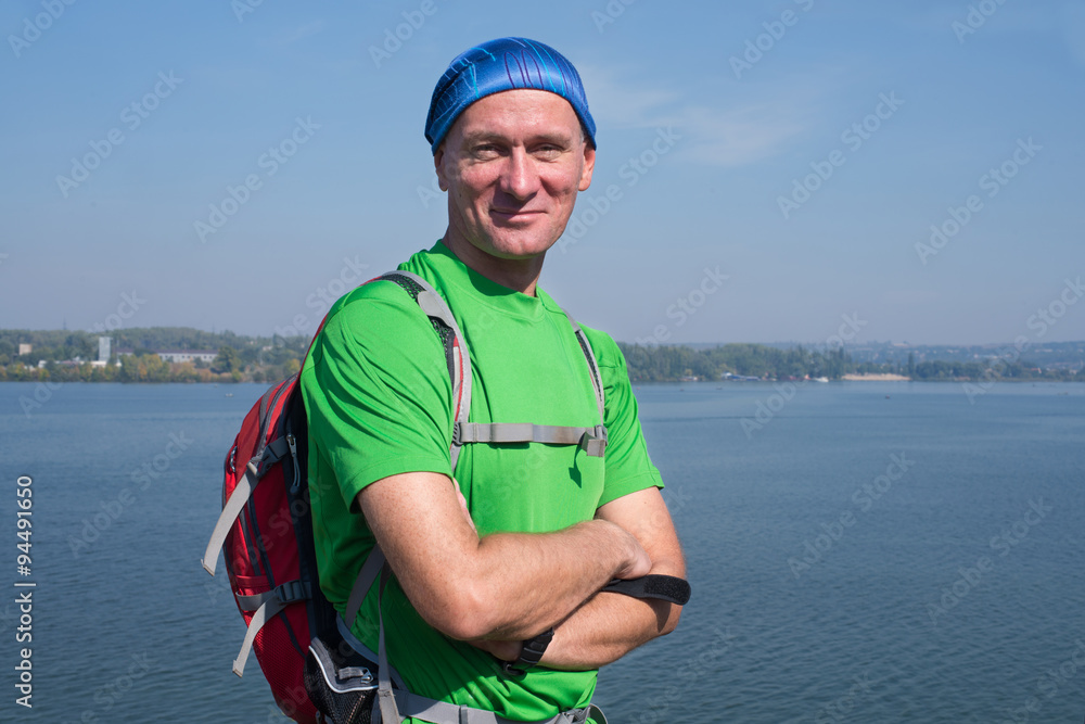 Hiker man with a backpack laughing, looking at camera on the bac